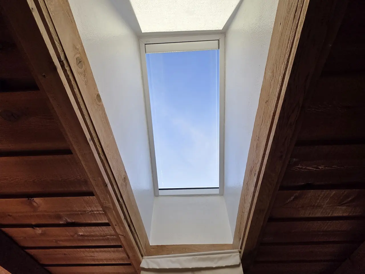 After: skylight shaft painted bright white against a wood-beam ceiling
